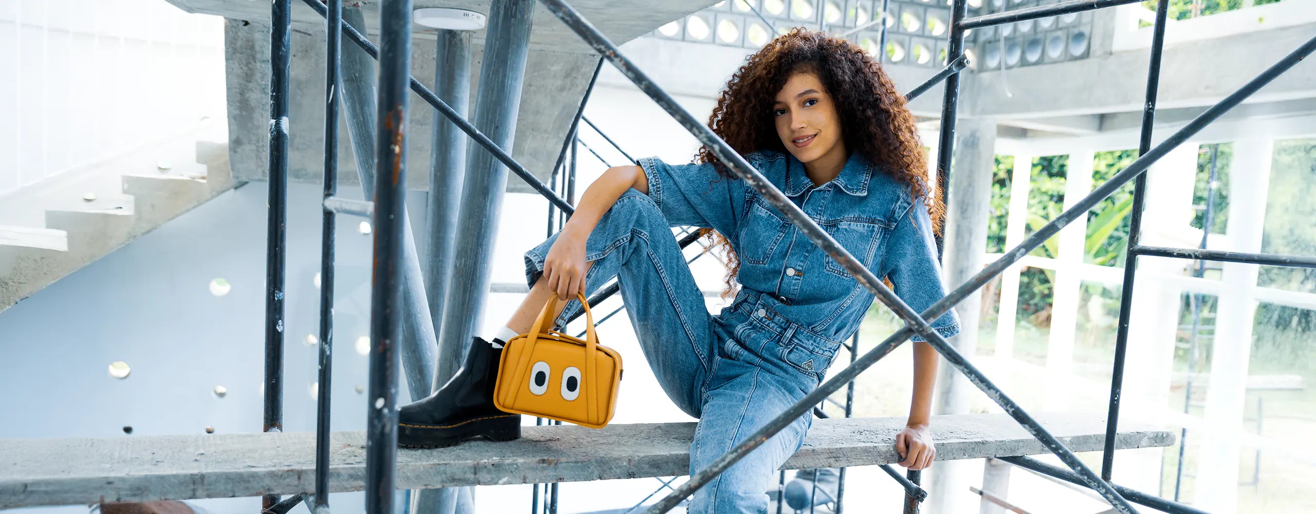 Yellow leather handbag with bold eye detail styled with denim in an industrial setting.