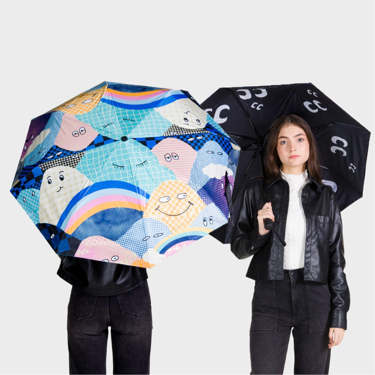 Min & Mon umbrellas with playful mountains faces and rainbow print next to a black umbrella with iconic eye symbols.
