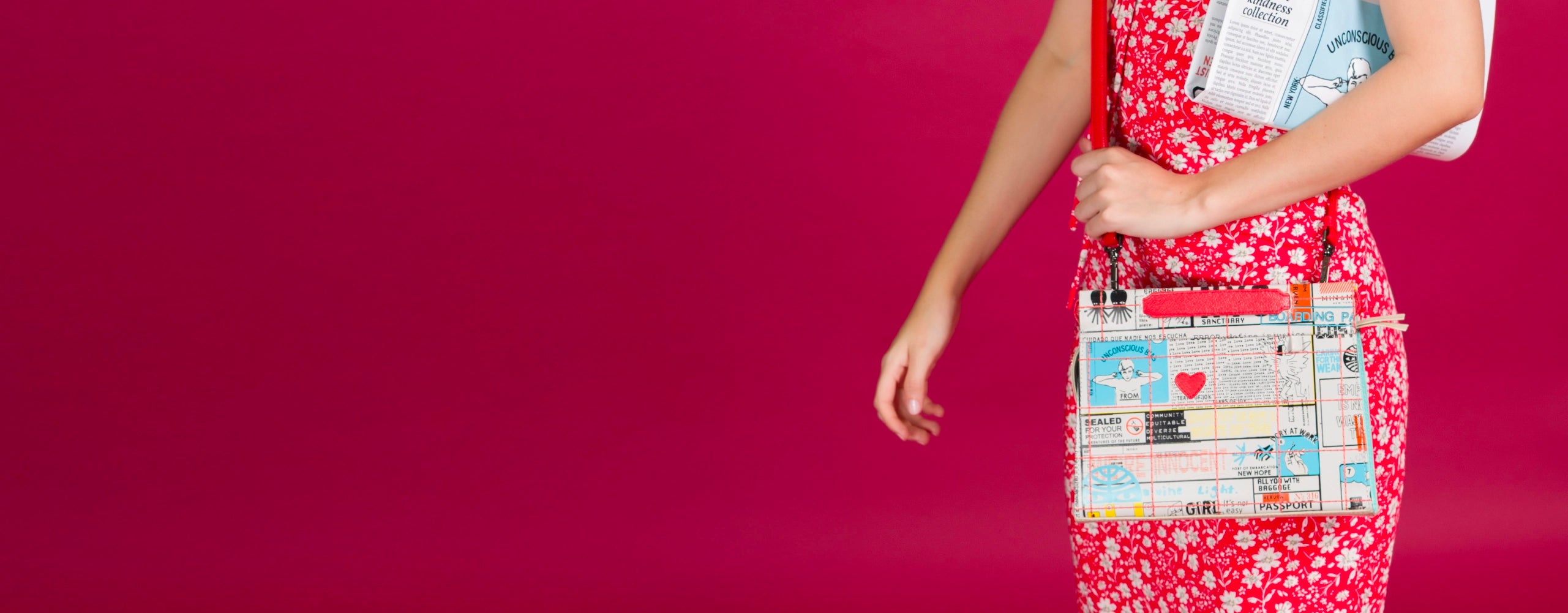 A woman in a red floral dress stands against a vivid pink background, holding a colorful crossbody bag with graphic newspaper-style prints, hearts, and whimsical elements. She tucks a folded newspaper titled “Classified Times” under her arm.