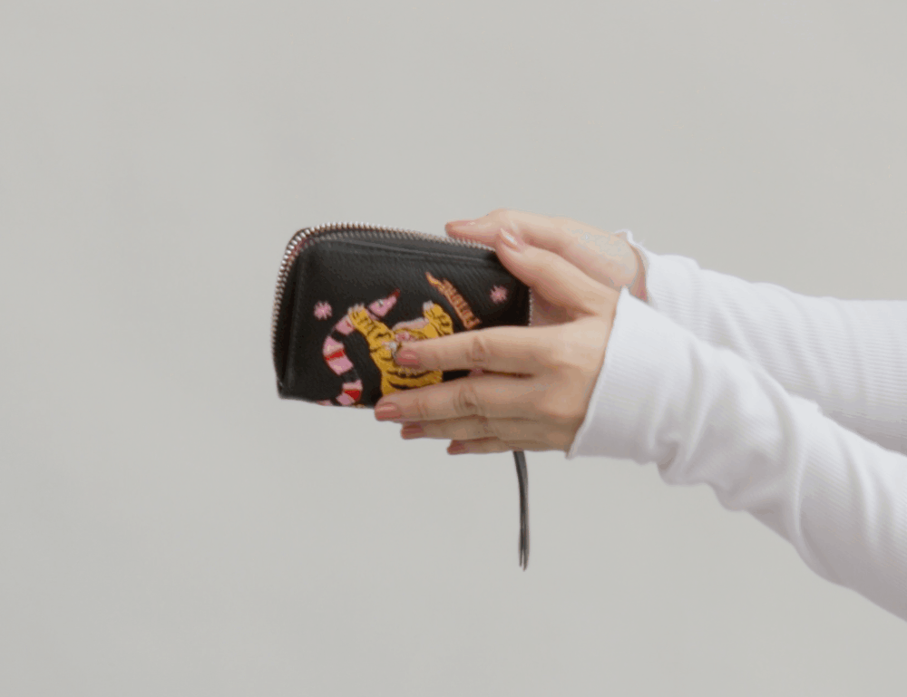 Opening of a zip-around black wallet with tiger and snake embroidery and pink interior.