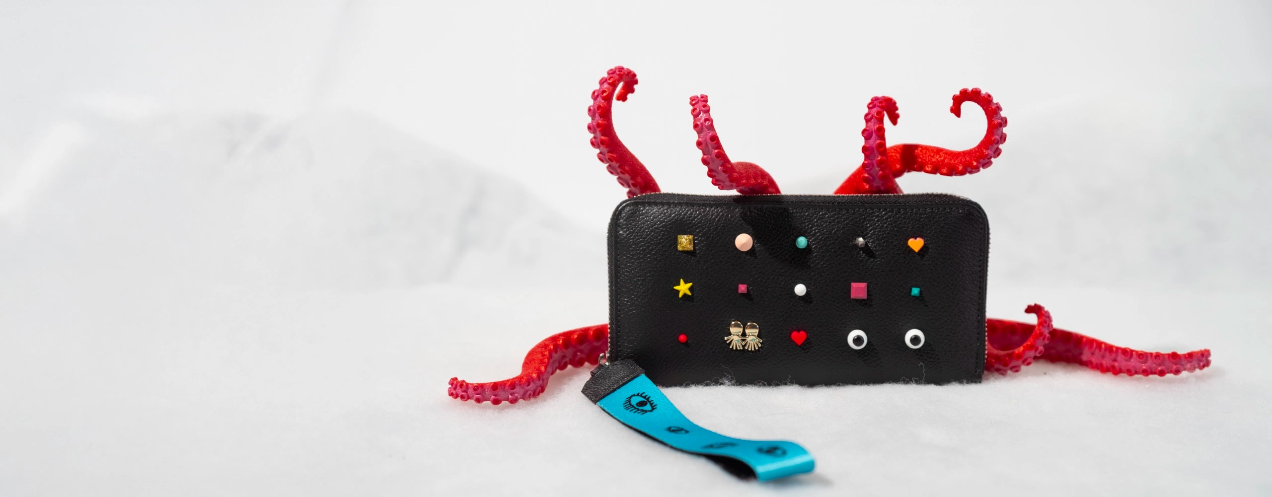 Black Min & Mon wallet decorated with colorful pins and red octopus tentacles, styled on a snowy white background.