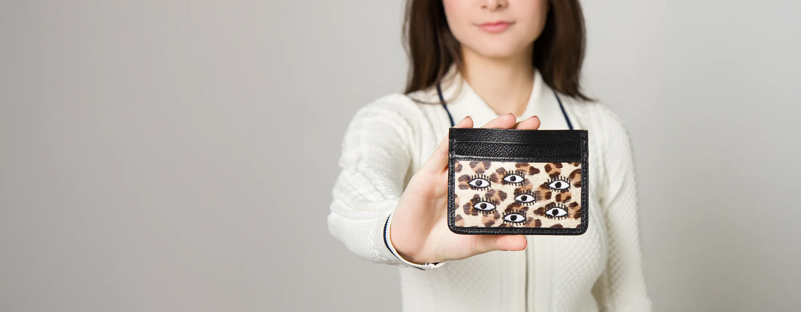 Close-up of a black leather cardholder wallet with leopard print and eye embroidery.