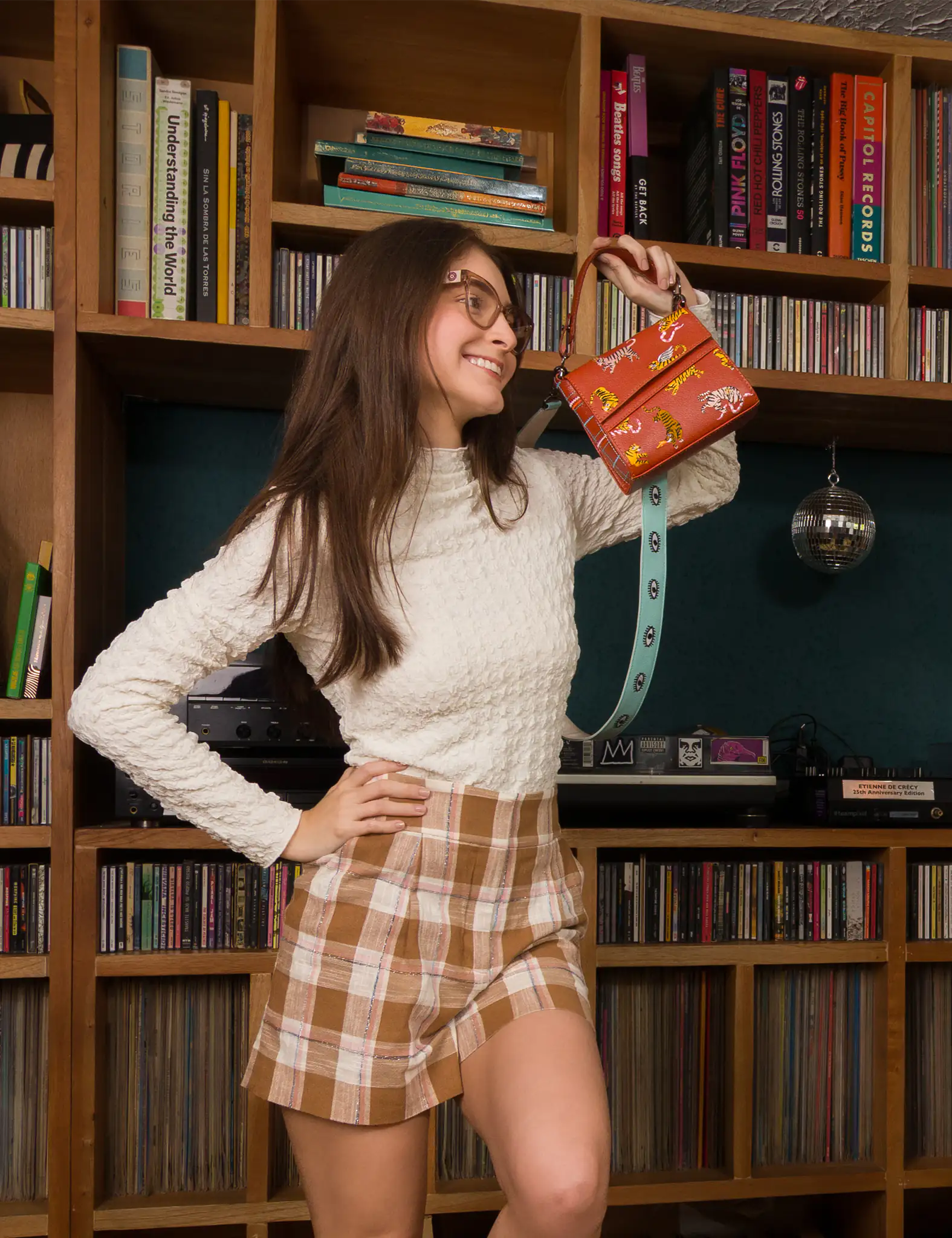 Woman holding a brown handbag in front of a bookshelf filled with books and CDs.