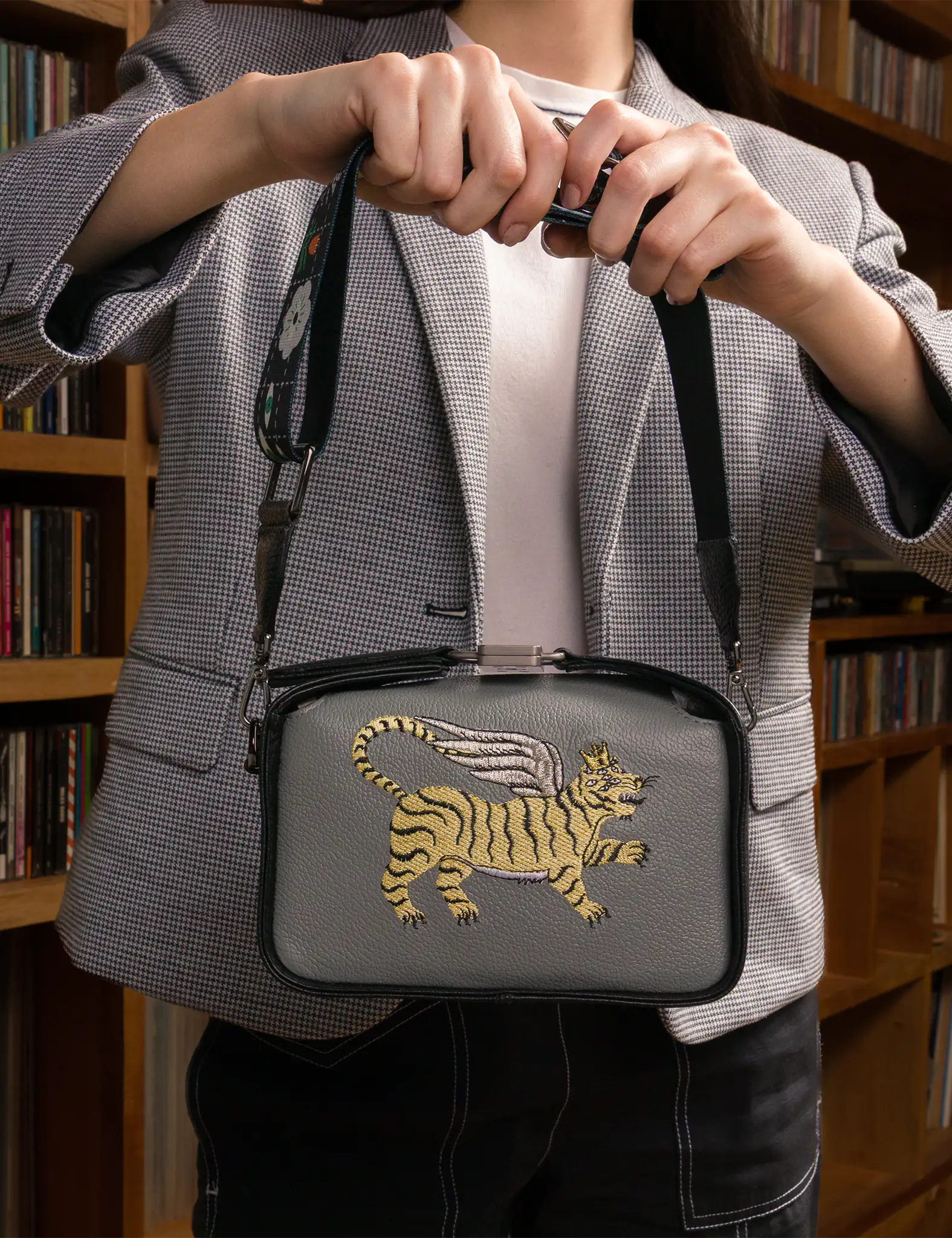 Woman holding a gray bag with a tiger design in front of a bookshelf.