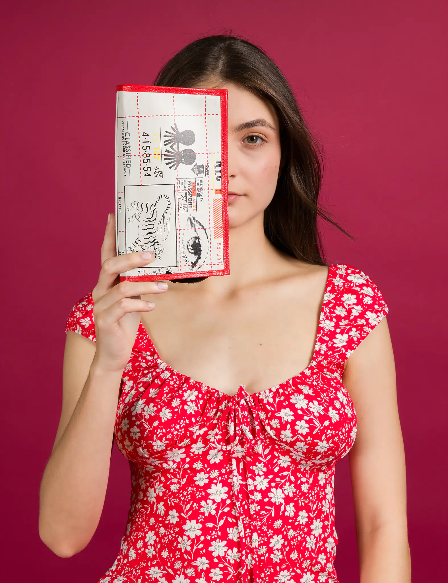 ChatGPT dijo:

Woman in a red floral dress holds a rectangular cosmetic case with red trim, decorated with black and white graphic prints of a tiger, eye, and text, against a red background.