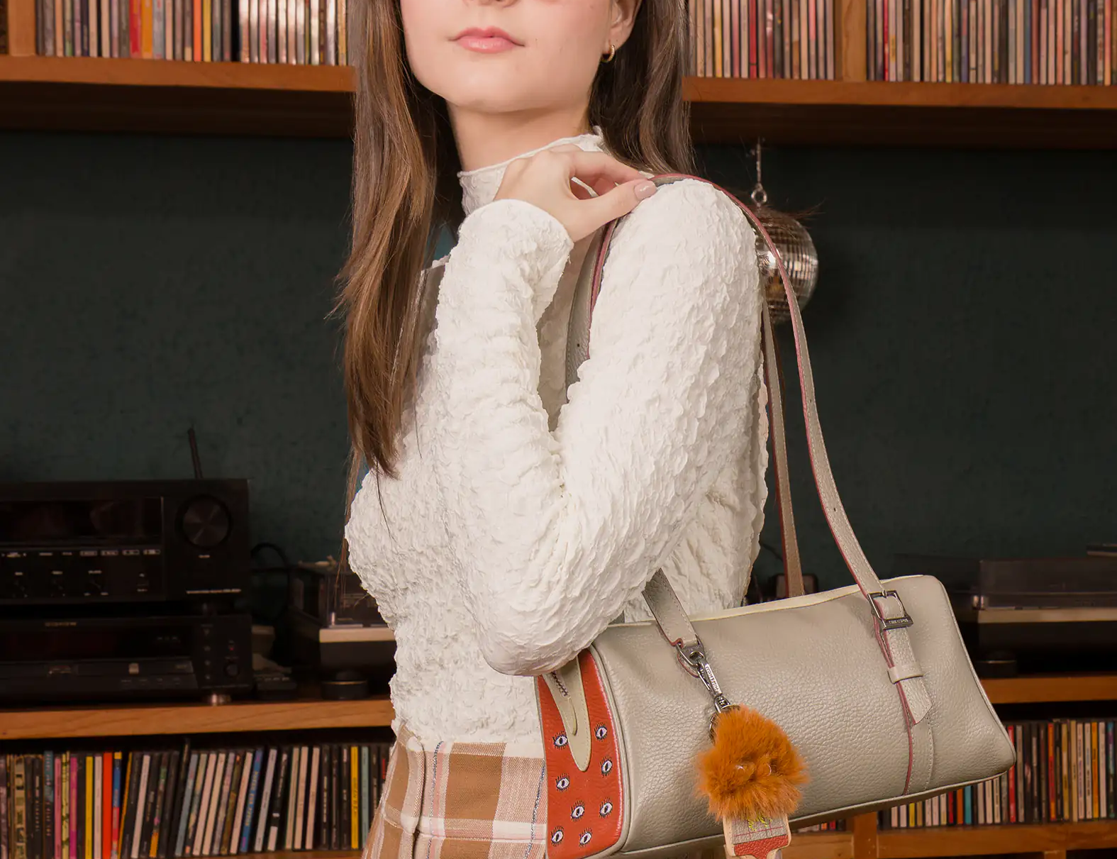 Woman holding a handbag in front of a bookshelf filled with records