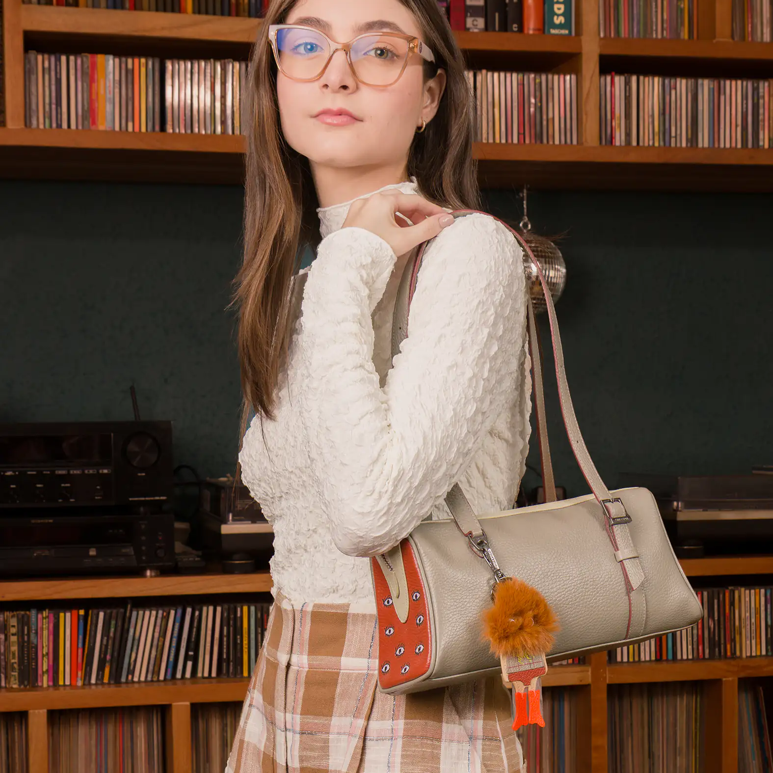 Woman holding a handbag in front of a bookshelf filled with records