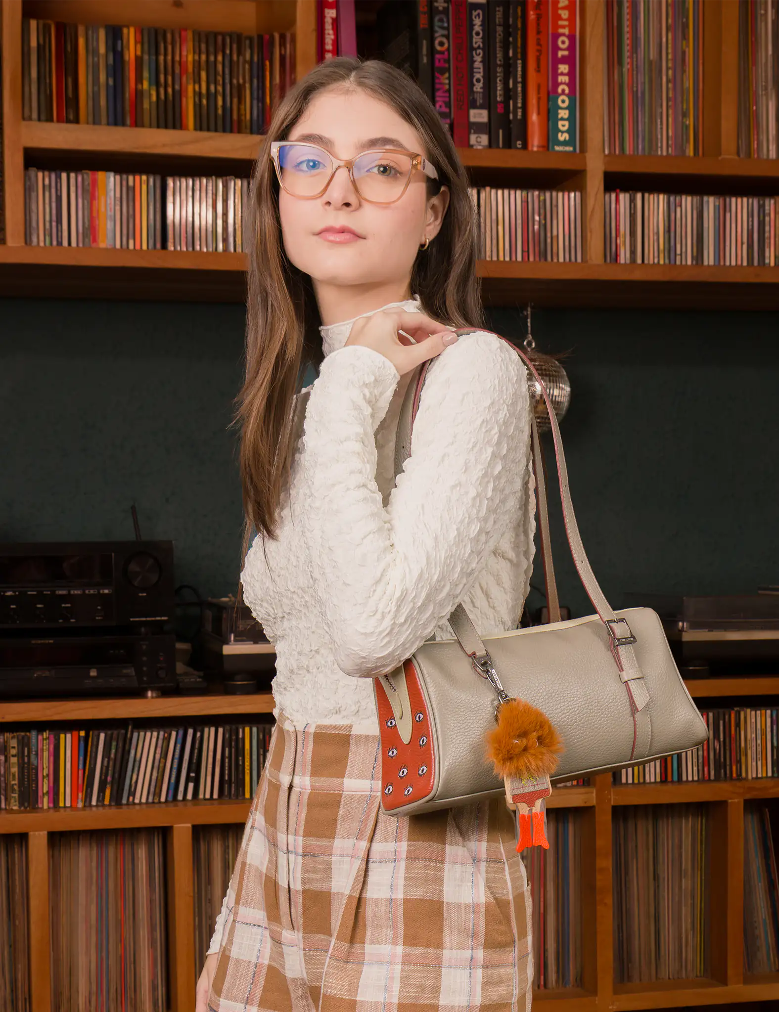 Woman holding a handbag in front of a bookshelf filled with records