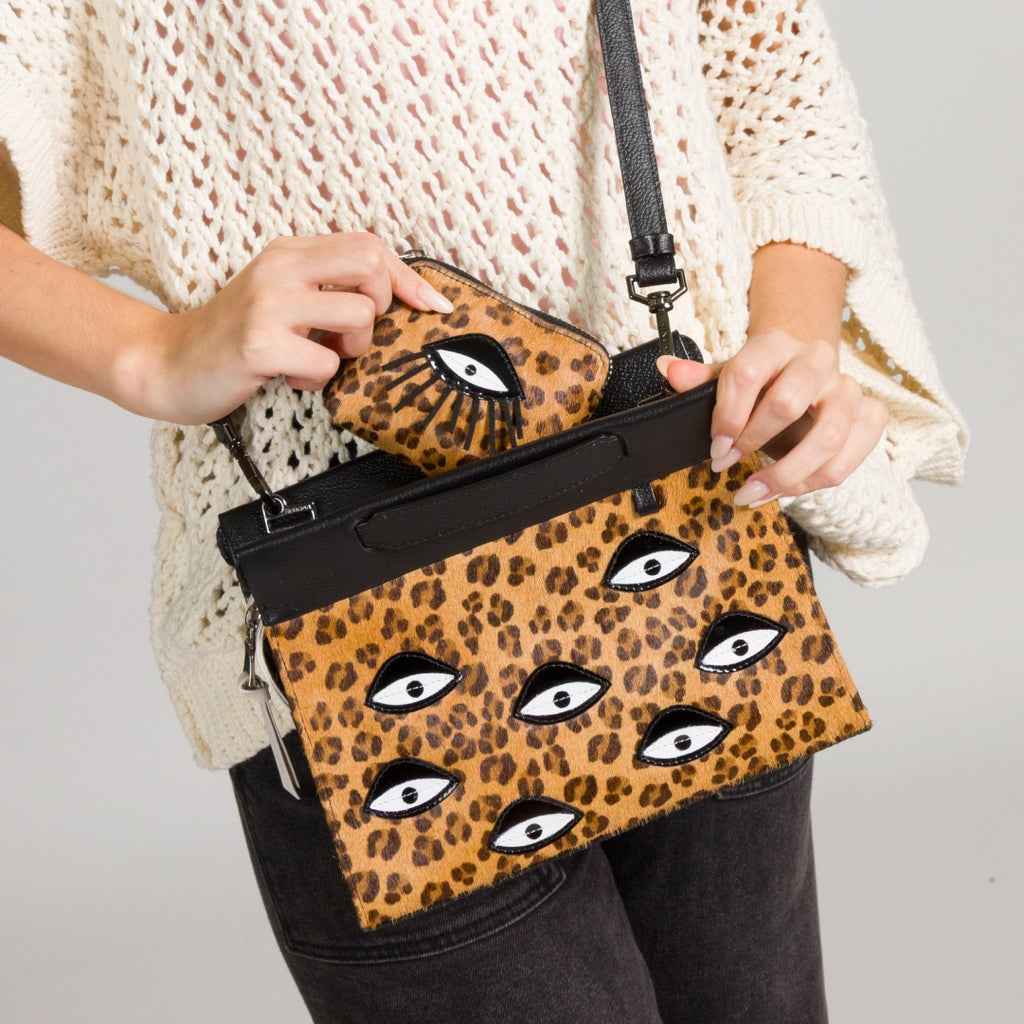 Close-up of a model holding a Min & Mon leopard-print handbag with embroidered eyes, placing a matching wallet inside.