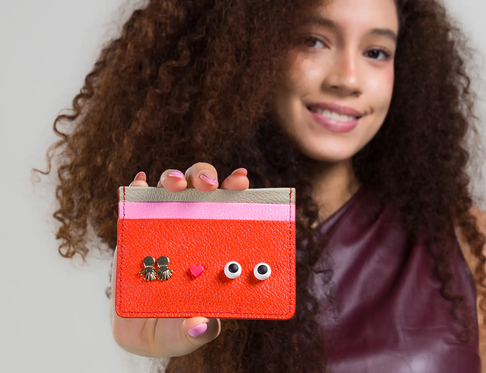 Young girl holding a red cardholder with decorative elements against a plain background