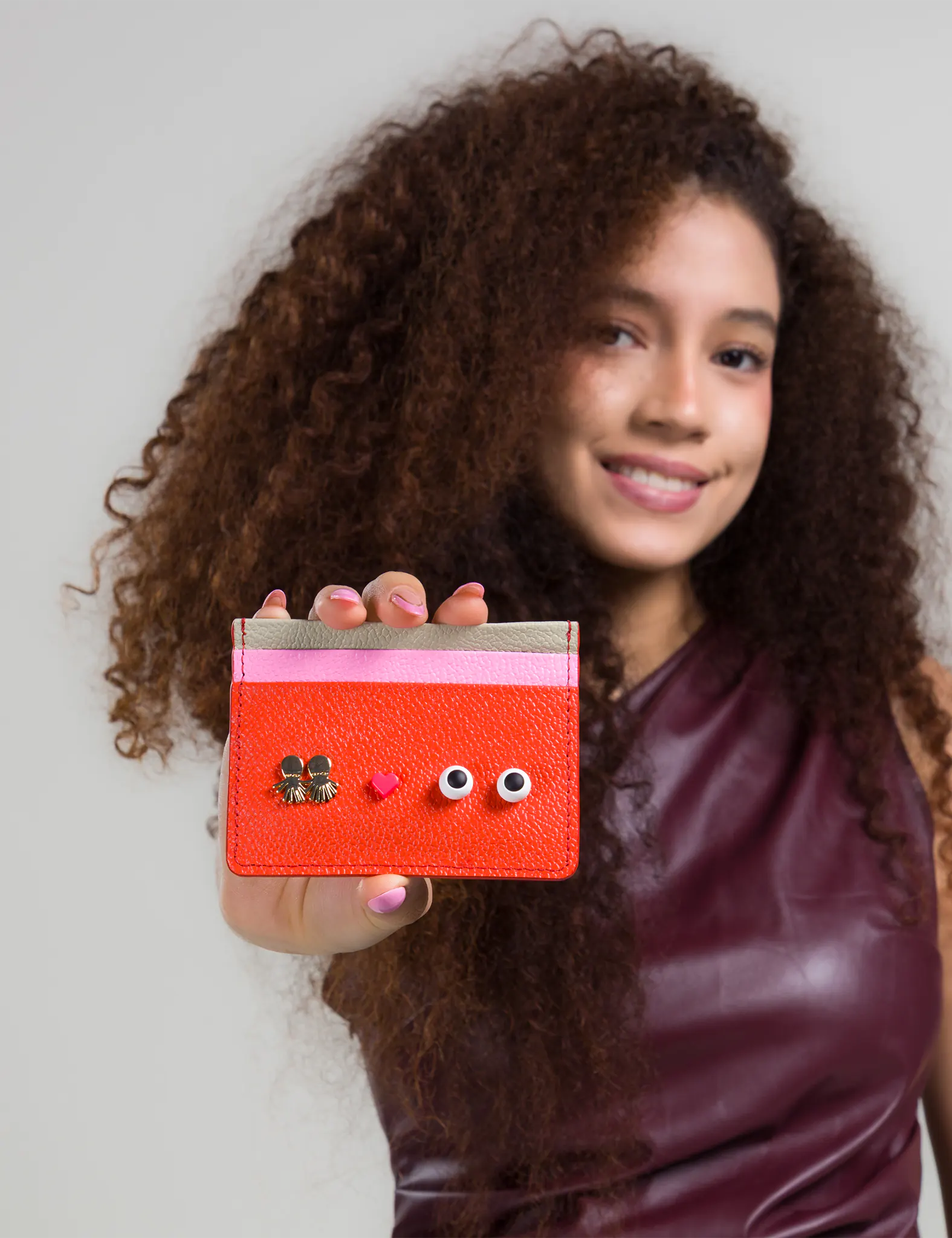 Young girl holding a red cardholder with decorative elements against a plain background
