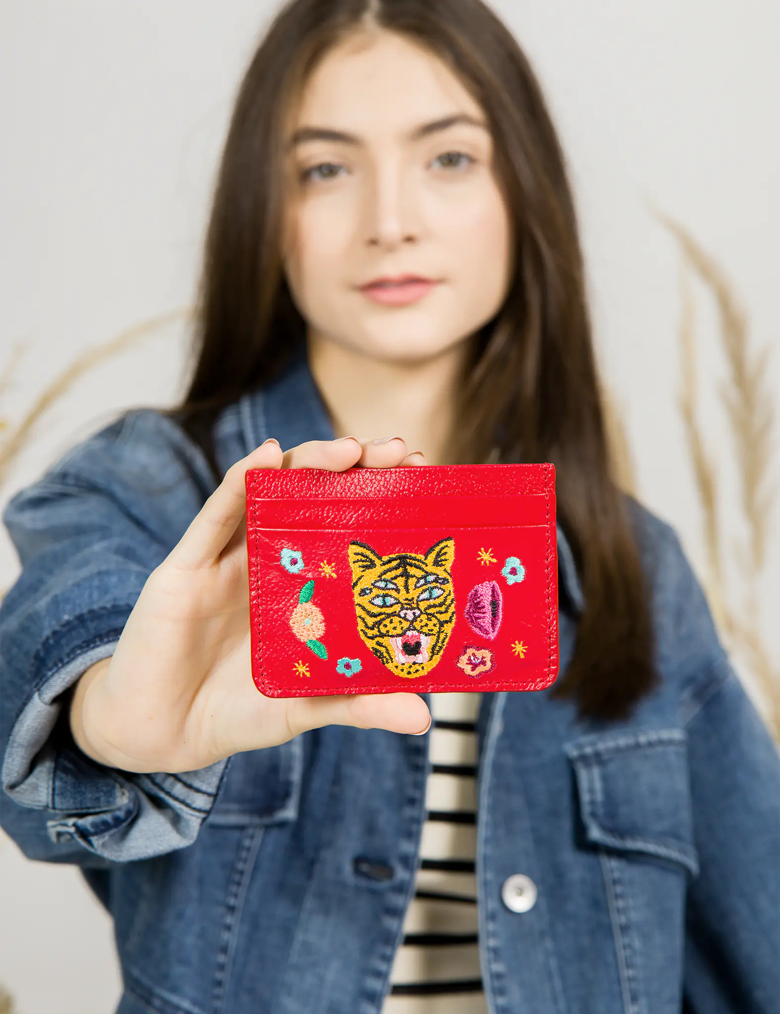 Woman holding a red cardholder with tiger and floral embroidery design.