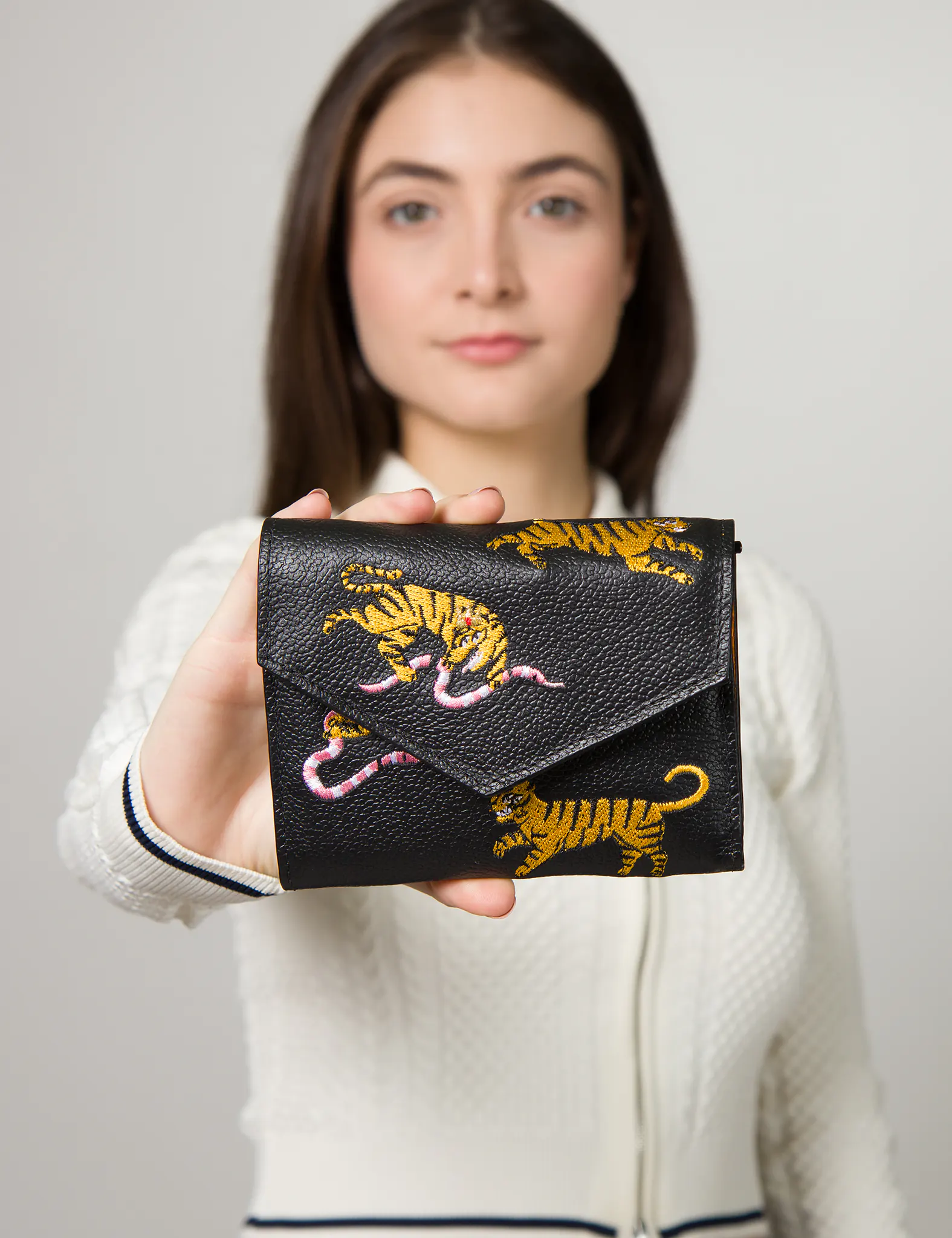 Close-up of a woman holding a black leather wallet with embroidered yellow tiger and pink snake design, featuring a flap closure.