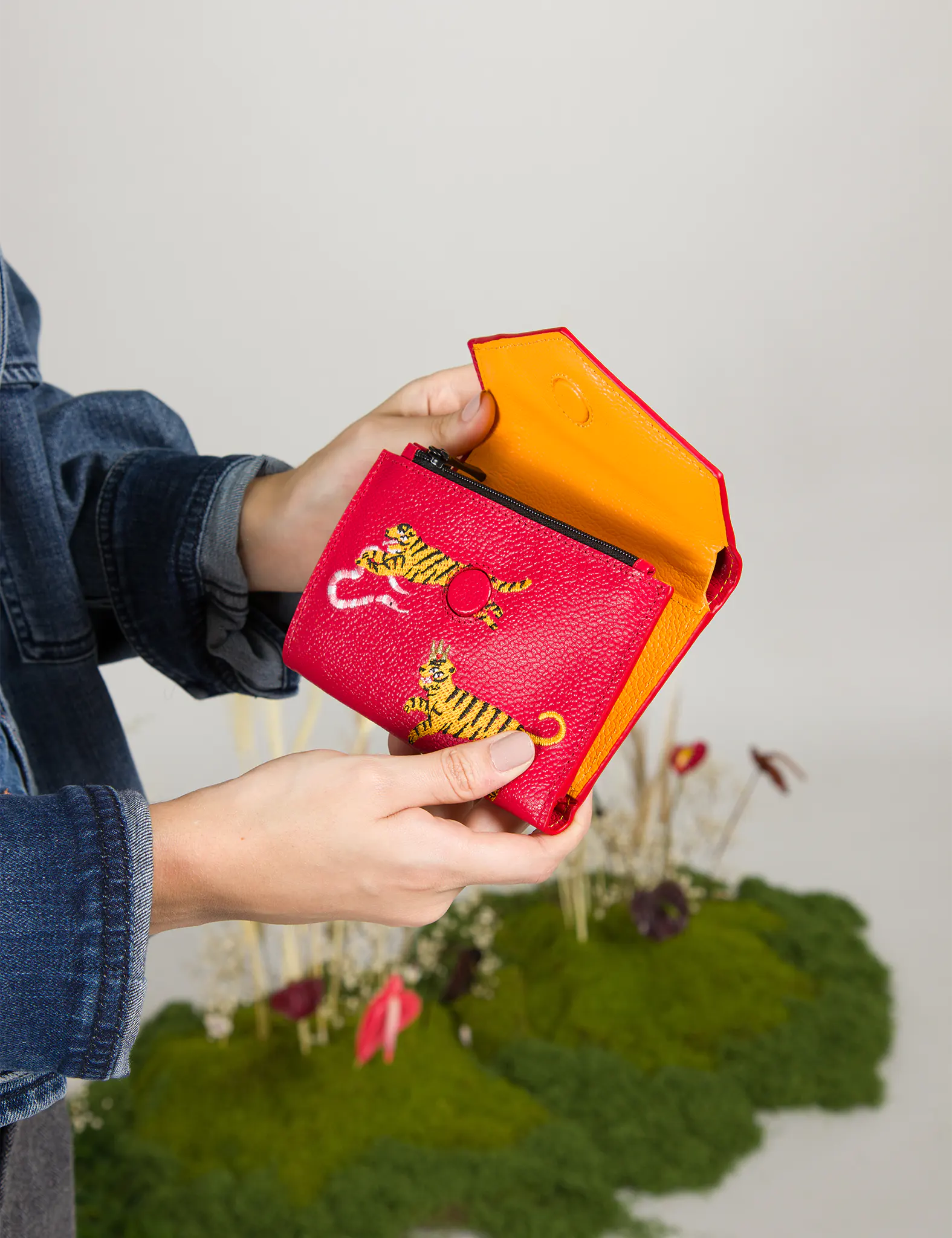Red wallet with yellow tiger design held by a person against a blurred natural background
