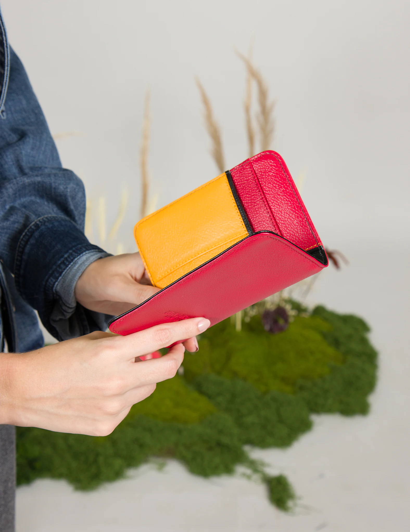 Close-up of a person holding an open red and yellow leather passport holder, showing its colorful two-tone interior design.