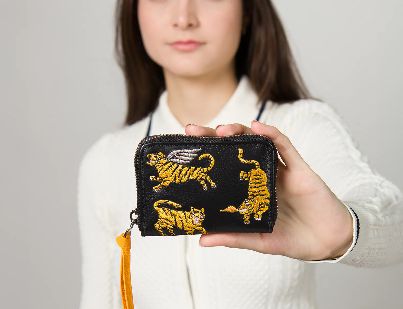 Person holding a black wallet with tiger designs against a plain background