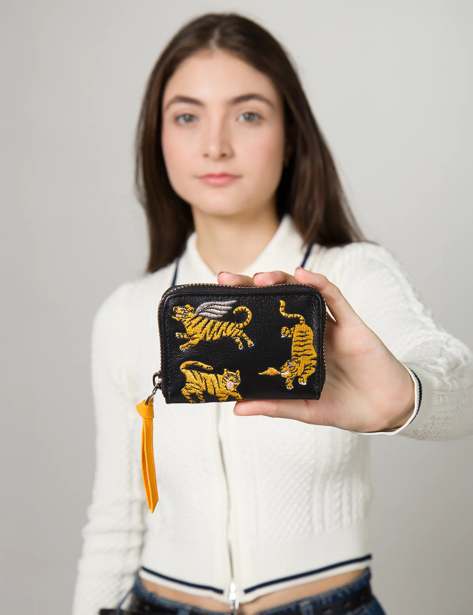 Person holding a black wallet with tiger designs against a plain background