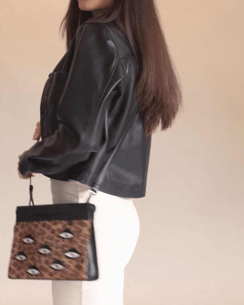 Animated GIF of a model dancing while wearing a black leather jacket and white dress, showing a Min & Mon leopard-print crossbody bag with embroidered eyes
