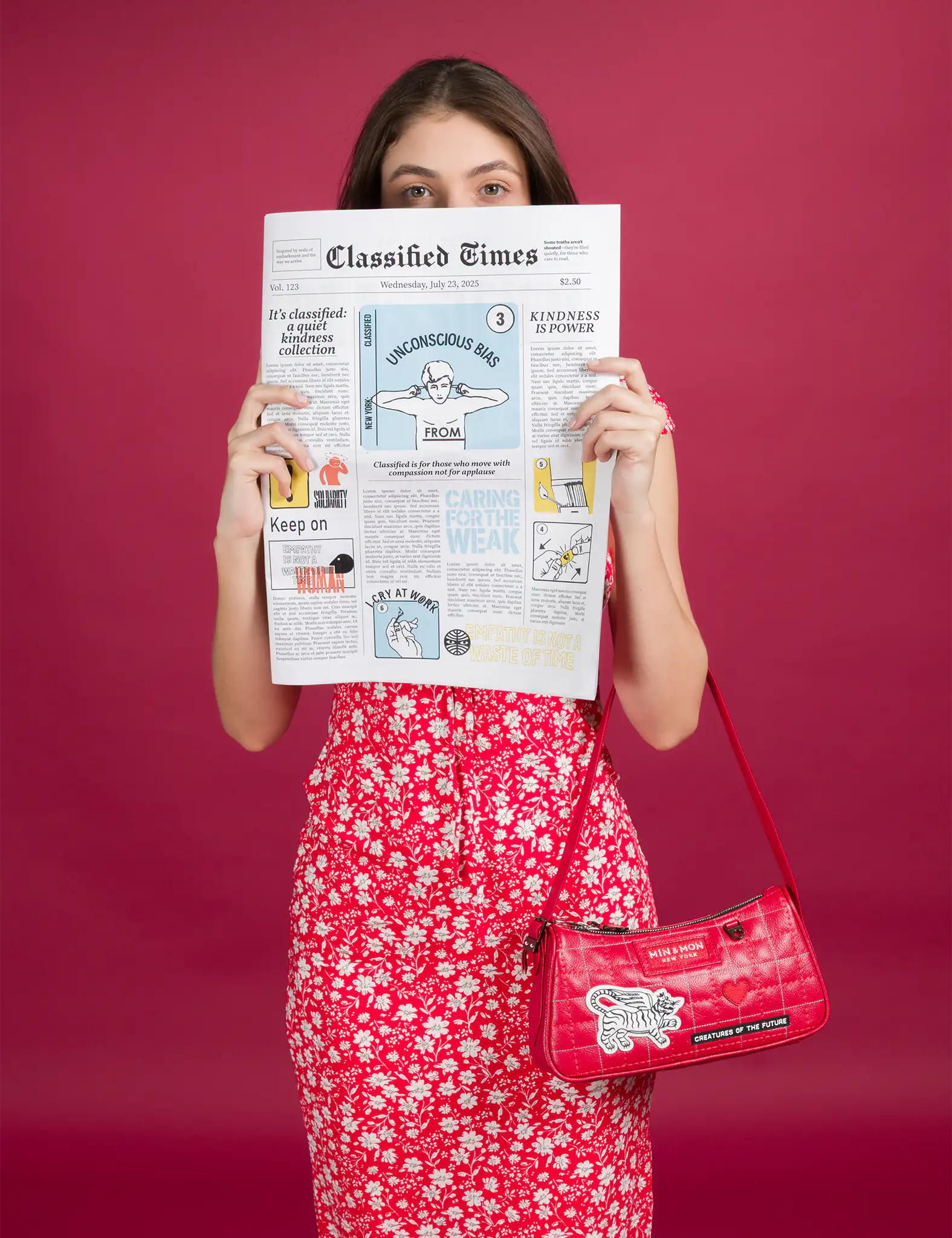 A woman in a red floral dress holds up a whimsical newspaper while carrying a vibrant red Min & Mon shoulder bag featuring a white tiger patch and the phrase “CREATURES OF THE FUTURE.”