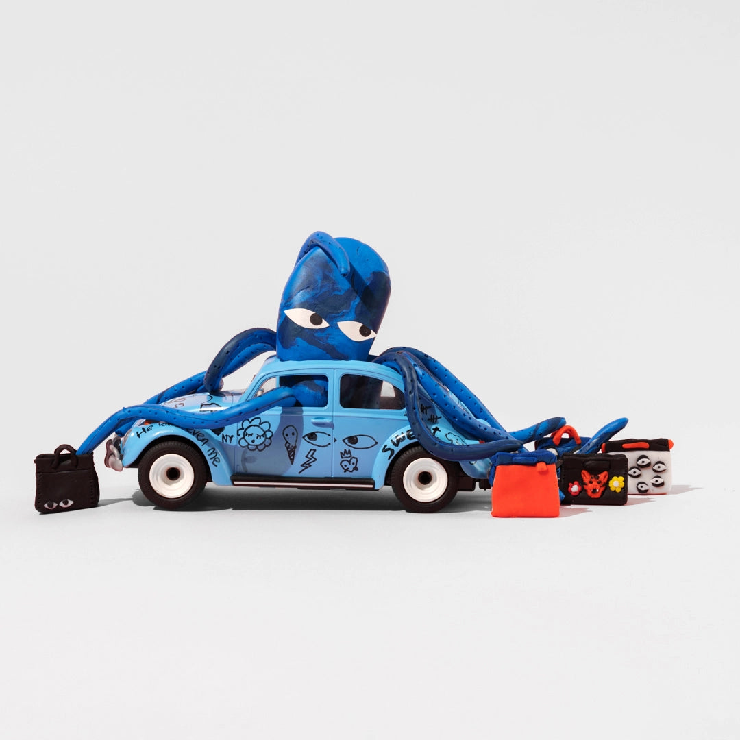  A whimsical scene featuring a blue toy car with various doodles and a blue octopus perched on top, holding multiple handbags by Min and Mon, an NYC-based brand. The background is white, highlighting the playful and creative design.