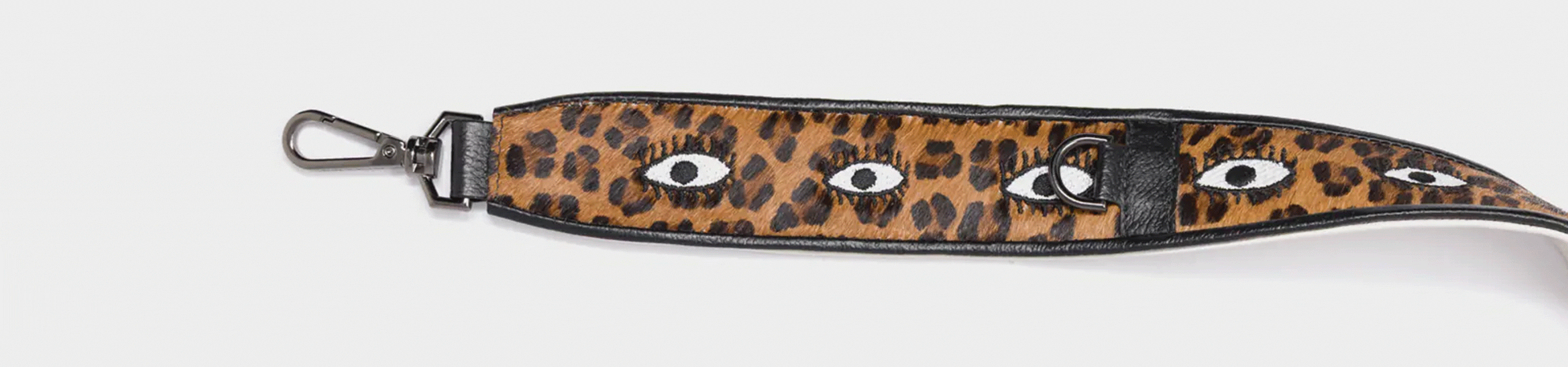 Close-up of a Min & Mon leopard-print bag strap with embroidered eyes in black and white on a brown background.