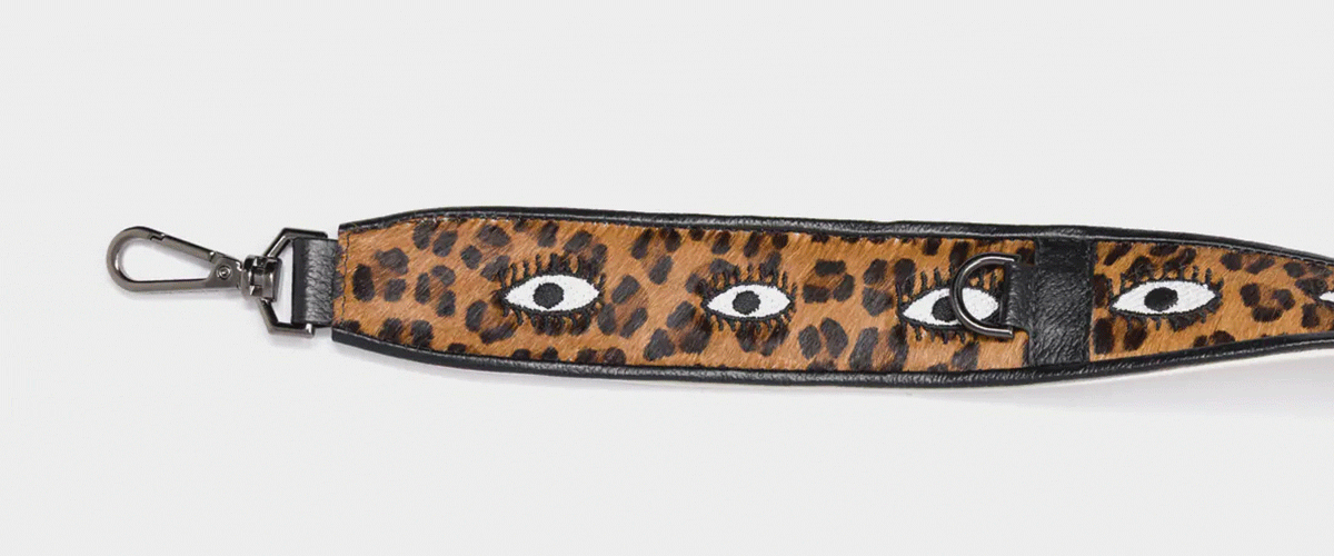 Close-up of a Min & Mon leopard-print bag strap with embroidered eyes in black and white on a brown background.
