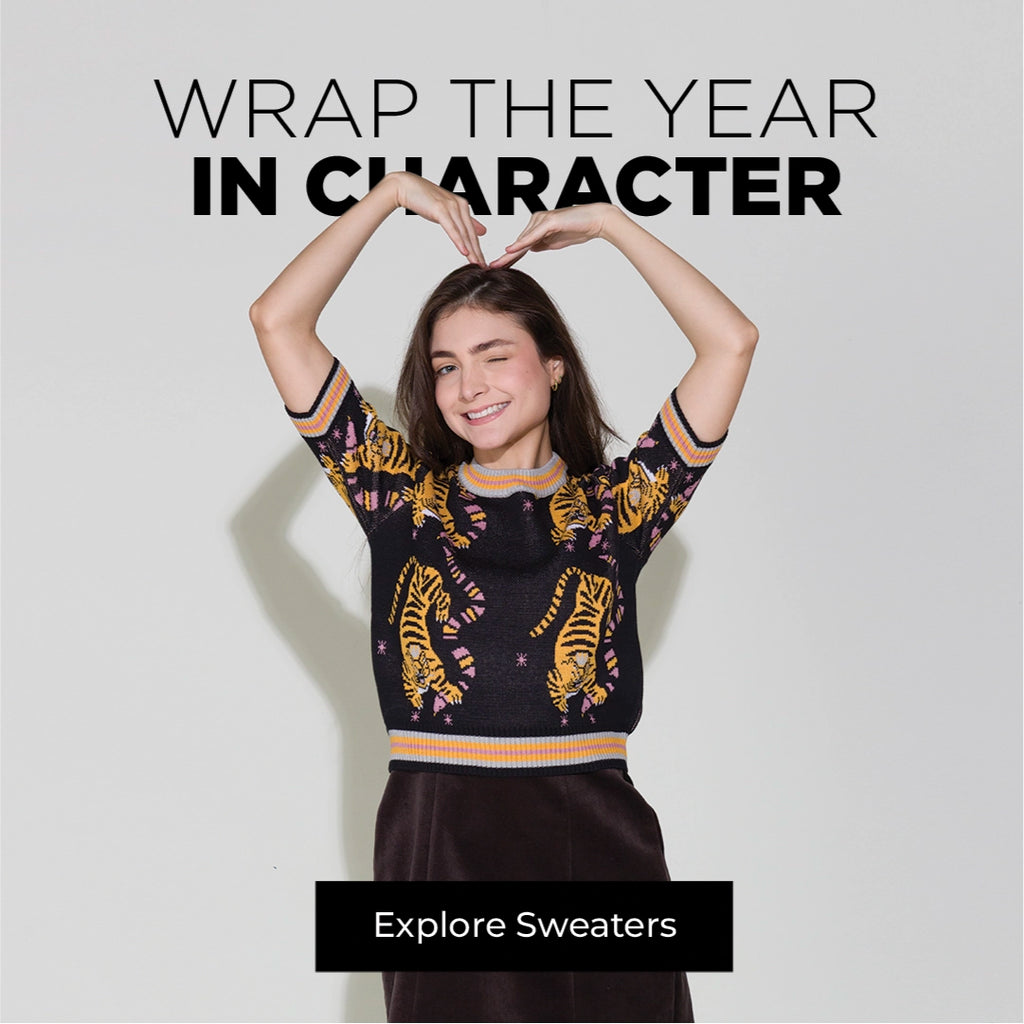 Model wearing a patterned Min & Mon sweater with the message “Wrap the Year in Character” and a button to explore sweaters.