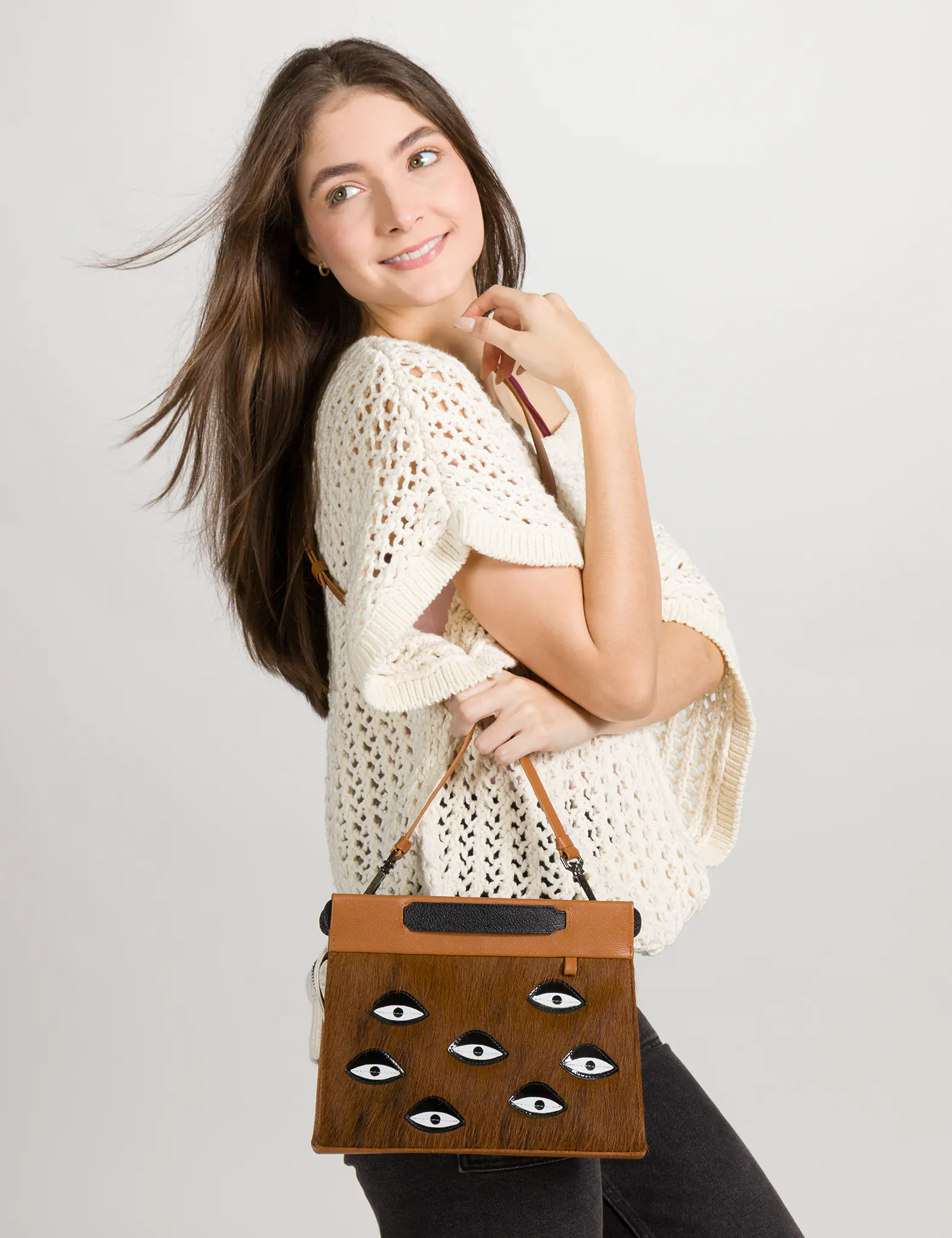 Woman holding a fur brown handbag with eye patterns on a plain background