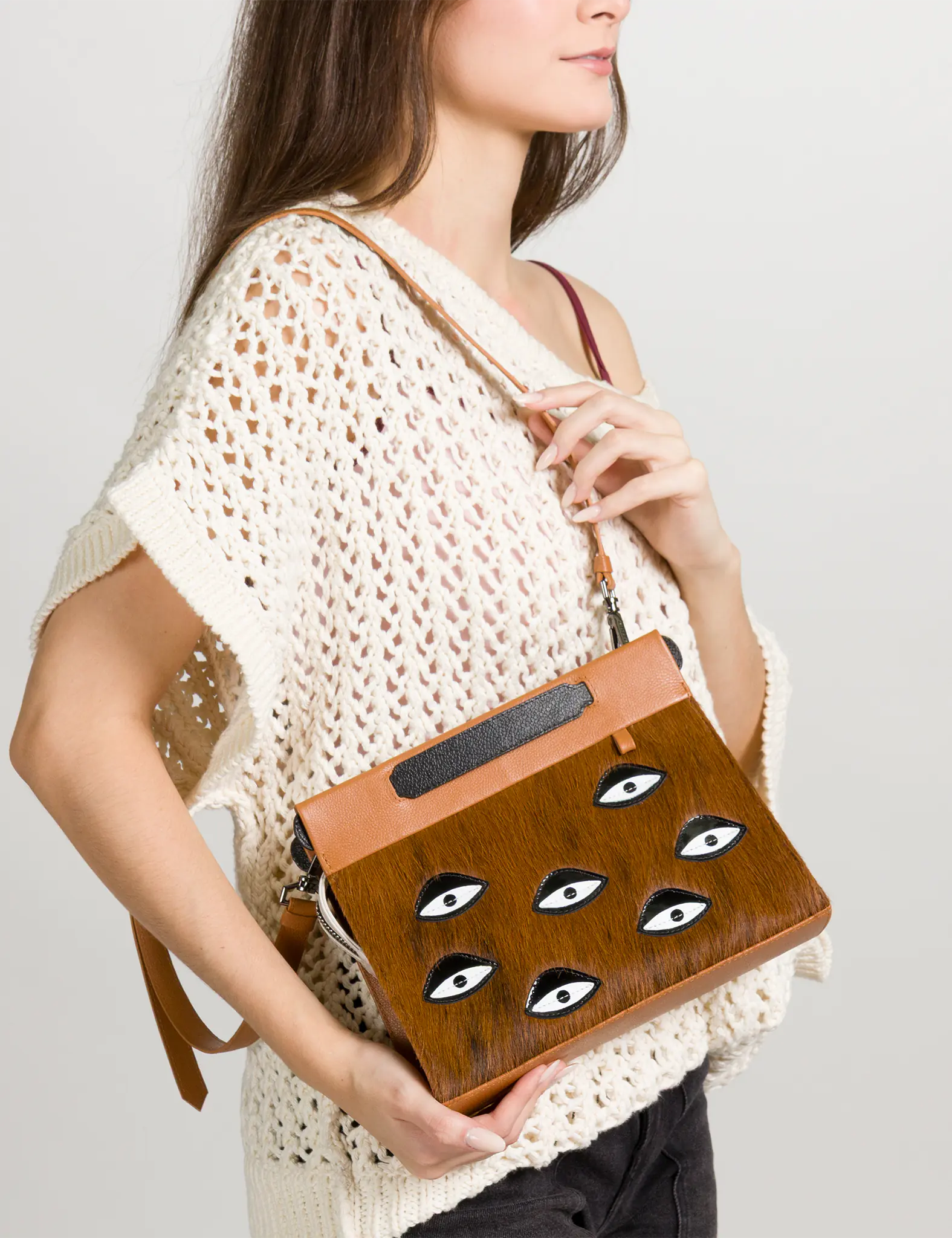 Woman holding a fur brown clutch with eye designs on a plain background