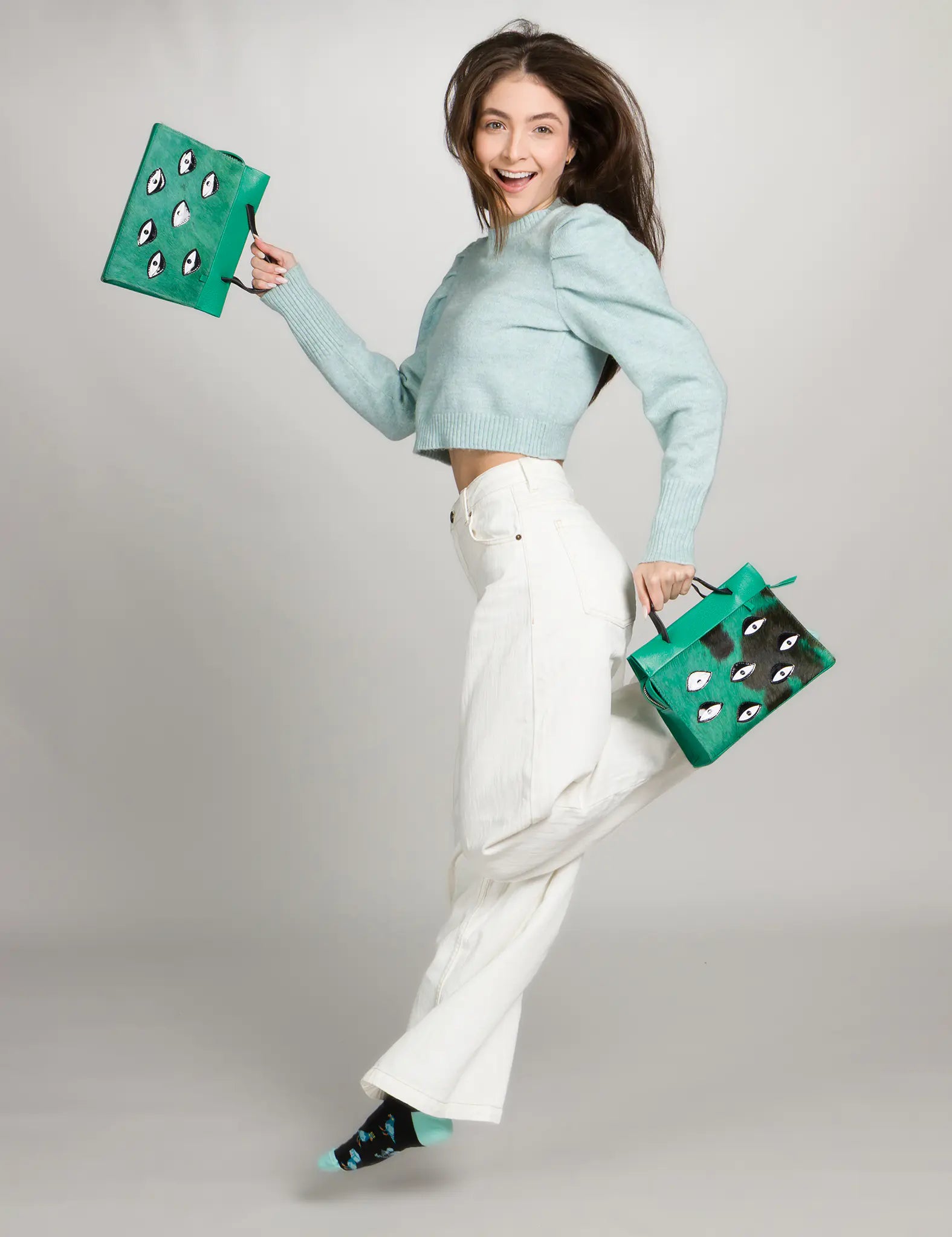 Woman holding two green handbags with eyes pattern against a gray background