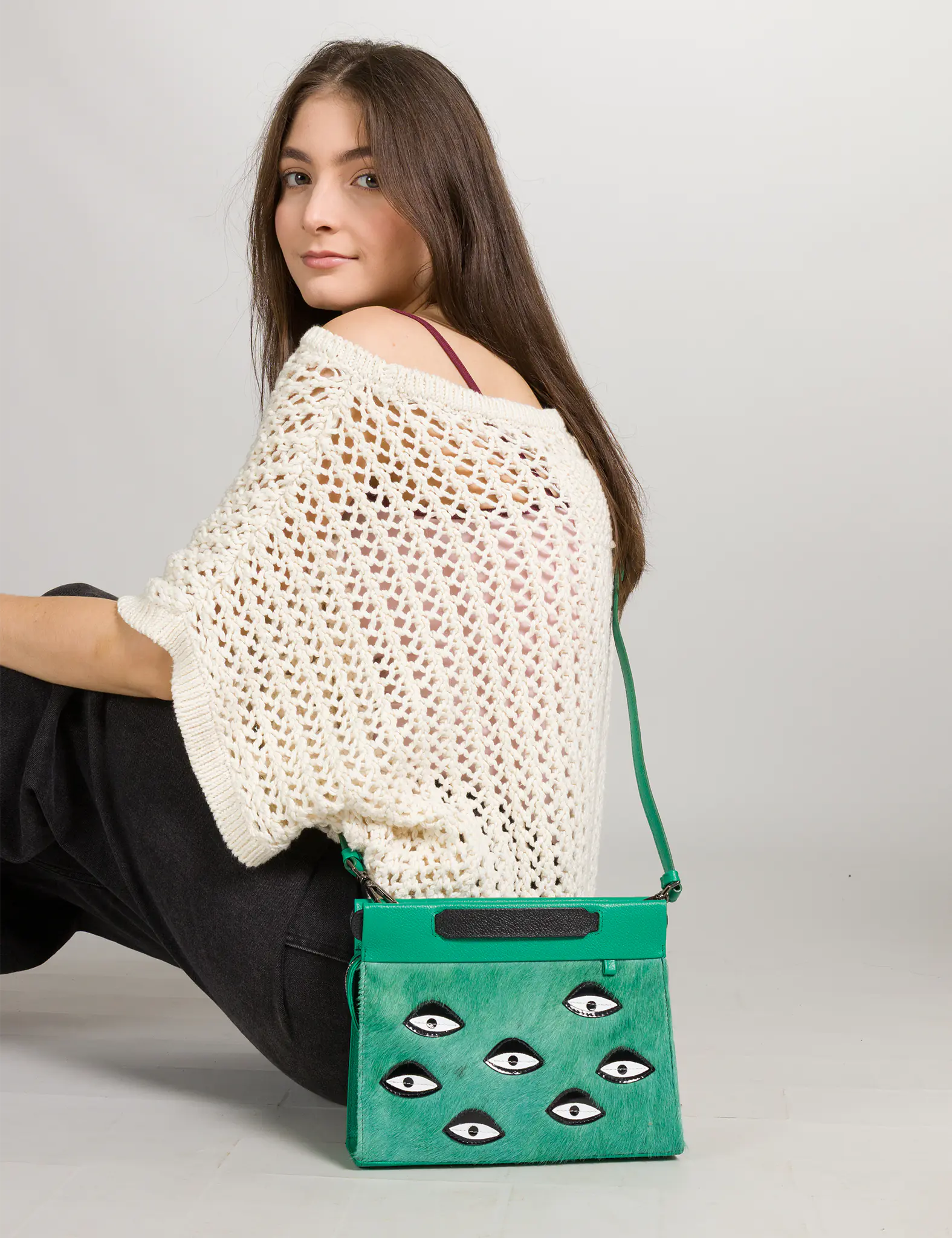 Woman holding a green handbag with eye designs on a plain background